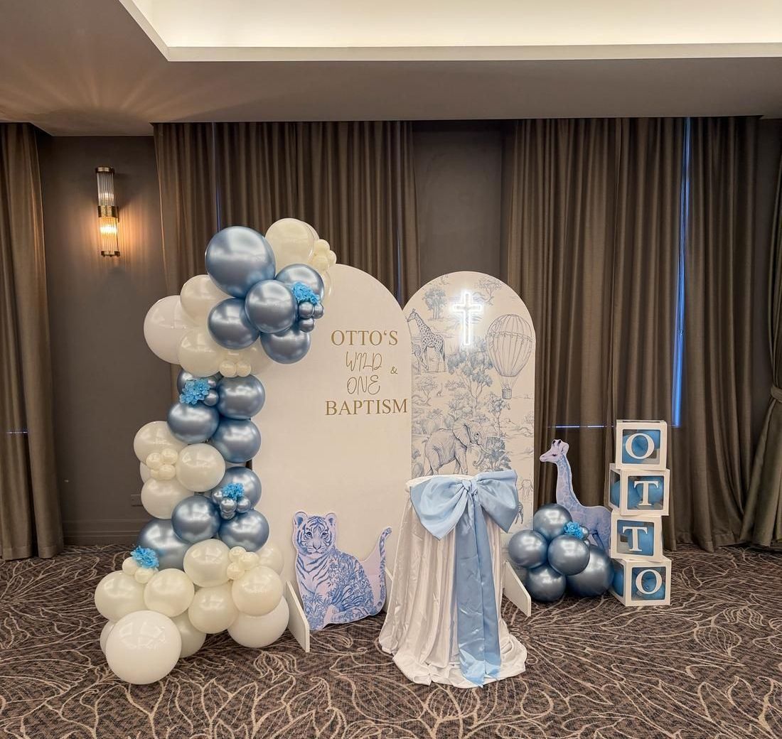 Blue and cream safari-themed balloon arch display with animal illustrations for a christening and first birthday celebration